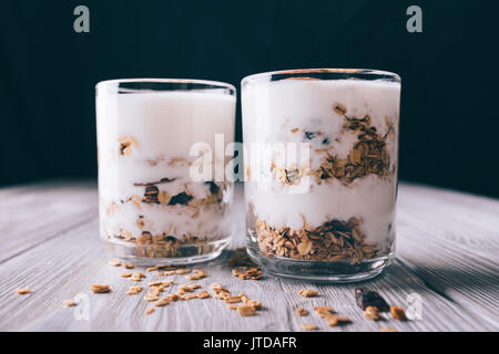 Joghurt mit Granulat in cups auf weißen Tisch und auf schwarzem Hintergrund. Gesunde vegetarische Nahrung. Stockfoto