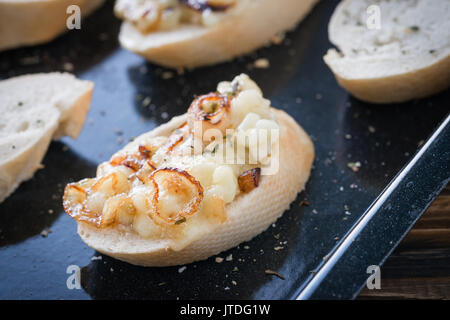 Baguette Scheiben mit hausgemachtem Käse Dip aus französischen Weichkäse aus der Region Bretagne oder Brie, karamellisierten Zwiebeln und getrocknete Kräuter, fertig zu backen. Stockfoto