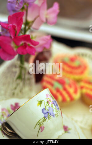 Eine Teetasse und eine Untertasse mit Blumendekor mit einigen Blumen auf einem Tisch für hohen Tee in einem traditionellen Ambiente. Stockfoto