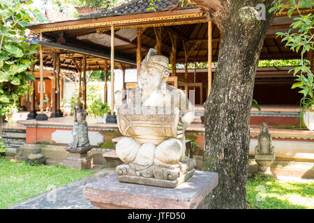 Balinesische Stein Skulptur eines Musikers vor einer traditionellen Balinesischen geschnitzten Holz Gebäude im Königlichen Palast, Singaraja, Bali Stockfoto