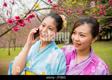 Nahaufnahme der Frau im Cherry Tree Garden können Sie über die mobile Handy zu sprechen sharing Kirschbäume blühen mit Freunden in Übersee reisen Stockfoto