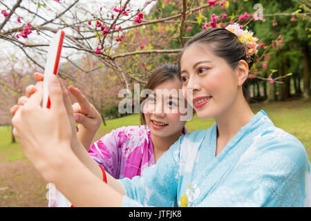 Weibliche Touristen Freundinnen zu Sightseeing in Japan voll Kirschblüten Blumen Garten und tragen Kimonos Kleider zeigen Mobiltelefon takin Stockfoto