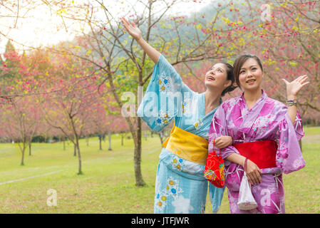 Süße lächeln Frauen in traditionellen Kimono Bekleidung Anzeige Geste genießen Cherry Blossom Blüte Bäume im Freien in Japan Reise Urlaub Stockfoto