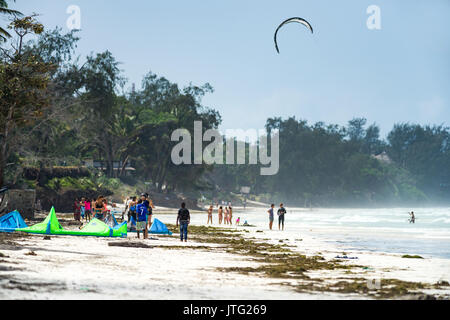 Touristen und Einheimische am Strand mit Kite Surfer, Diani, Kenia Stockfoto