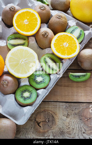 Frische saftige Zitrusfrüchte in einer Box Fach auf einer hölzernen Hintergrund Kiwi, Orange, Zitrone, Grapefruit Stockfoto