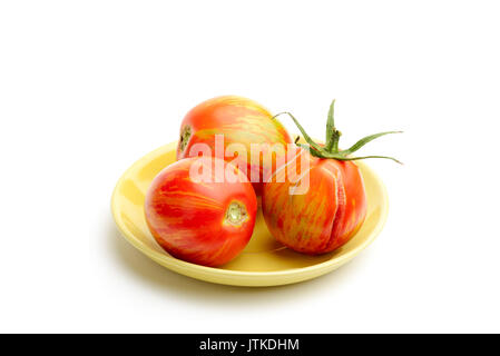 Drei saftige rote zebra Tomaten in einem kleinen gelben Porzellan Teller, auf weißem Hintergrund Stockfoto