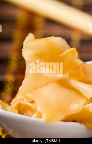 Nahaufnahme der einige Scheiben eingelegter Ingwer in eine weiße keramische Schüssel, auf einen Tisch für Mittag- oder Abendessen Stockfoto