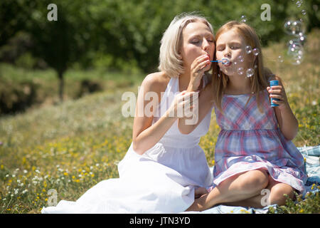 Schöne junge Mutter Blasen Blasen mit ihrer Tochter. Stockfoto