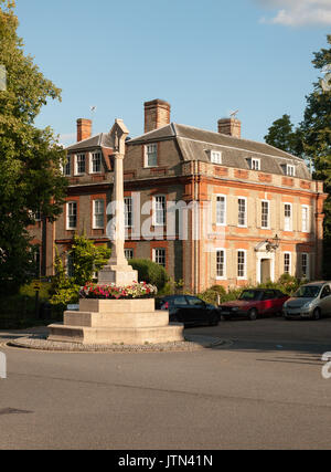 Ein kriegerdenkmal Wahrzeichen vor ein herrschaftliches Haus in Dedham mit einigen geparkten Autos im Sommer Licht; UK Stockfoto