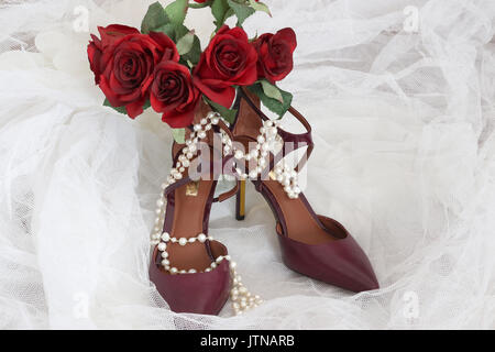 Helle Schuhe für stilvolle Braut. Burgund Farbe hohen Hügel Paar schicke Schuhe und Bräute Blumenstrauß mit rote Rosen auf einem weißen Bridal Veil. Stockfoto