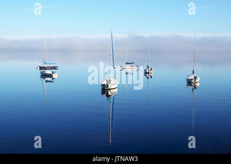 Schöne Misty Morning Sunrise. Landschaft mit einem Segel Boote in einer ruhigen Oberfläche des Sees reflektiert und ein Nebel über Wasser. Horizontale Composit Stockfoto