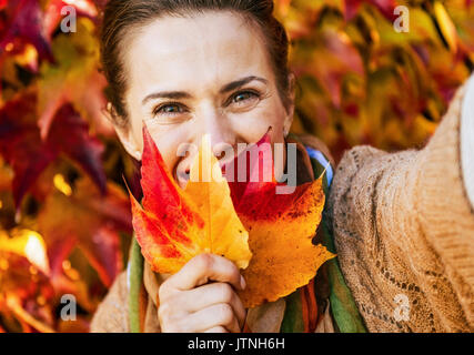 Glückliche junge Frau versteckt sich hinter Blatt gleichzeitig Selfie vor Herbstlaub Stockfoto