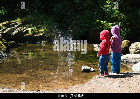 Zwei kleine Kinder werfen Steine ins Wasser Stockfoto