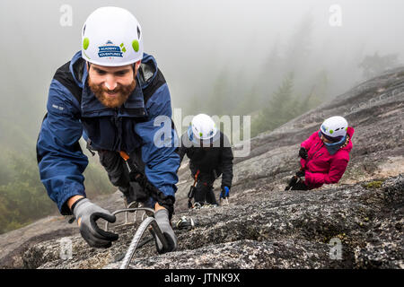 Ein Mann erreicht für die Metall- rung beim Klettern Klettersteig in Squamish, British Columbia. Stockfoto