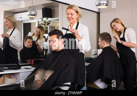 Lächelnde ältere blonde Frau Haare schneiden der indischen Kerl in Barbershop Stockfoto