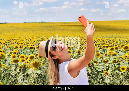 Fröhliches Mädchen unter selfie in einem blühenden Sonnenblumen Feld Stockfoto