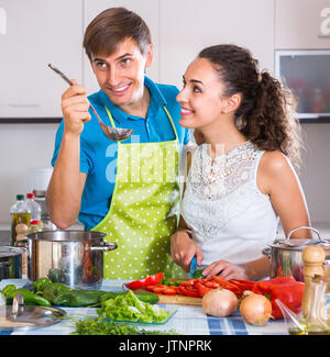 Glückliche junge Mann in Schürze helfen lächelnde Frau vegetarische Suppe vorbereiten Stockfoto