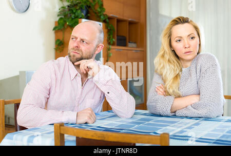 Mann und Frau in einen Streit. Sie sitzen am Tisch drehte sich von einander entfernt. Fokus auf Mann Stockfoto