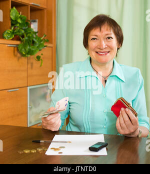 Lächelnd gealterte Frau am Tisch sitzend mit Geld und Dokumente Stockfoto