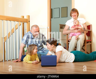 Glückliche Familie, der mit einem tragbaren Computer auf dem Boden zu Hause Innenraum Stockfoto