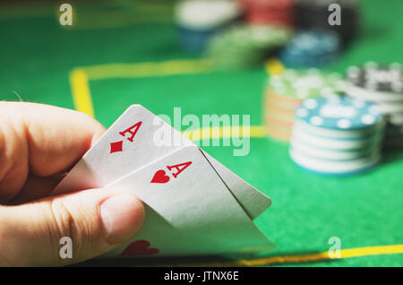 Zwei rote Asse in der Hand. Grün Pokertisch mit Chips unscharf im Hintergrund Stockfoto