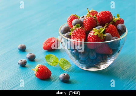 Beeren in eine Glasplatte auf einem blauen Hintergrund Holz. Blick von oben auf die Erdbeere und Heidelbeere in Glasschale auf runden Platte Matte, selektiver Fokus der Mix fr Stockfoto