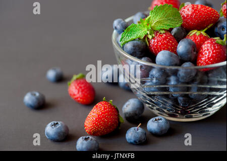 Glas Schale mit frischen Bio Blaubeeren, Brombeeren, Himbeeren und Erdbeeren garniert mit Minze gefüllt Stockfoto