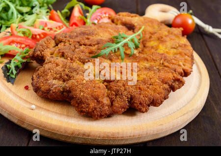 Eine große Wiener Schnitzel und Salat auf einem Schneidebrett auf einem dunklen Hintergrund. Nahaufnahme Stockfoto