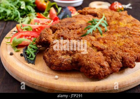 Eine große Wiener Schnitzel und Salat auf einem Schneidebrett auf einem dunklen Hintergrund. Nahaufnahme Stockfoto