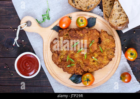 Eine große Wiener Schnitzel auf einem Schneidebrett auf einem dunklen Hintergrund. Ansicht von oben. Stockfoto