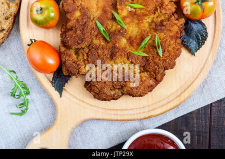 Eine große Wiener Schnitzel auf einem Schneidebrett auf einem dunklen Hintergrund. Ansicht von oben. Stockfoto