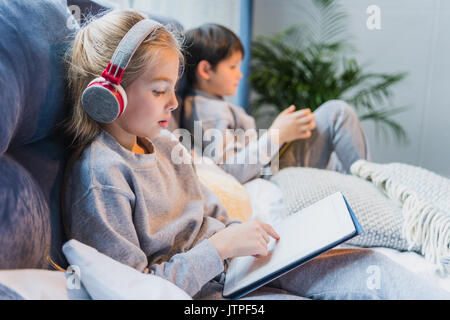 Seitenansicht der fokussierten Mädchen im Kopfhörer und kleinen Jungen mit digitalen Tabletten Stockfoto