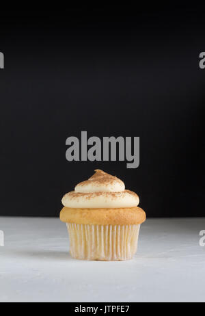 Cup Cake Hintergrund mit einem Cupcake auf weißem gekrönt mit Zimt Pudding auf rustikalen Weiß mit Defokussierten schwarzen Hintergrund - Platz für Text