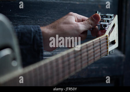 Kaukasische männliche Hand Tuning eine akustische Gitarre auf schwarzem Hintergrund aus dunklem Holz mit selektiven Fokus Stockfoto