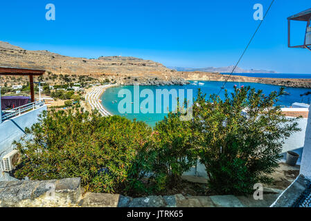 Kleine Bucht in Lindos auf der Insel Rhodos Griechenland überfüllt mit Sonnenschirmen, wie Boote und Schwimmer geniessen Sie die Bucht und das Mittelmeer an einem heißen Tag Stockfoto