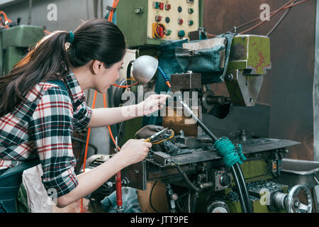 Rückansicht Foto von elegante Frau Drehmaschine Arbeiter an Fräsmaschine Abteilung und mit Hilfe einer Zange Werkzeug einstellen Komponenten arbeiten. Stockfoto