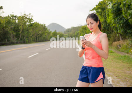 Schöne weibliche joggen Läufer tragen smartwatch stehen auf der Straße Street können Sie über Handy Kontakt sms mit Freunden nach Abschluss marat Stockfoto