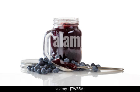Blueberry jam in Löffel mit frischen Reifen Blaubeeren und Jar im Hintergrund. Auf weiß mit Reflexion isoliert. Stockfoto