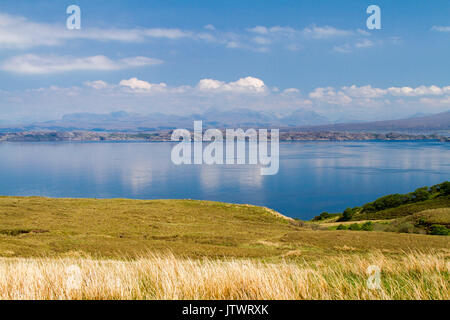 Blick von der Isle of Skye über ruhige, blaue Meer zum Festland und in den Bergen von Schottland unter blauem Himmel. Stockfoto