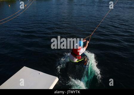 Junger Mann, der durch die Kabel gezogen auf Wakeboard in See Stockfoto