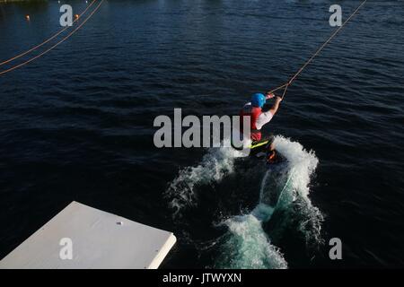 Junger Mann, der durch die Kabel gezogen auf Wakeboard in See Stockfoto