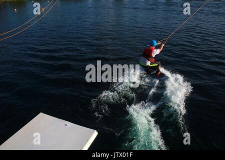 Junger Mann, der durch die Kabel gezogen auf Wakeboard in See Stockfoto