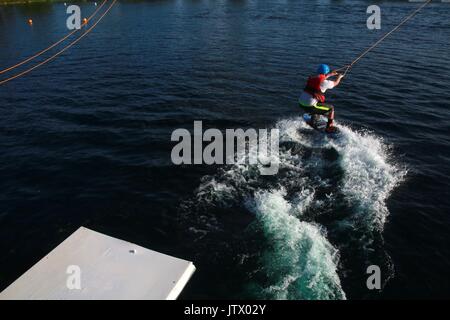 Junger Mann, der durch die Kabel gezogen auf Wakeboard in See Stockfoto