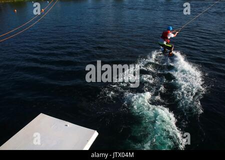 Junger Mann, der durch die Kabel gezogen auf Wakeboard in See Stockfoto