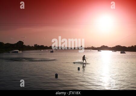 Wake Boarder Schlittschuhlaufen auf dem See bei Sonnenuntergang über Rot abgestufte Filter Sky akzentuieren Stockfoto