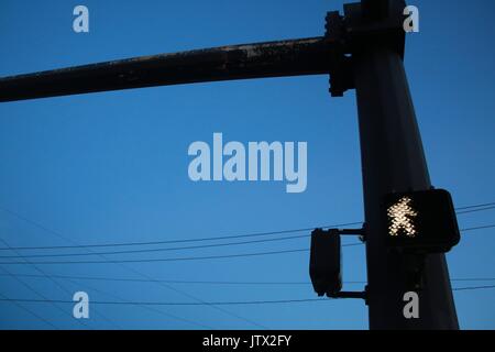 Weiß beleuchtete Spaziergang Symbol auf Ampel an der Kreuzung mit Stromleitungen im Hintergrund nach Einbruch der Dämmerung gegen blauen Himmel Stockfoto