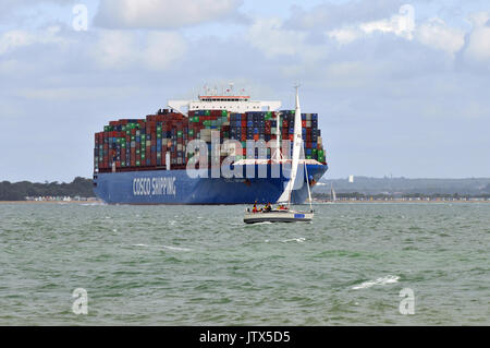 Ein großes Containerschiff navigatimg Southampton Wasser thorn Kanal in Cowes auf der Isle of Wight mit einer Yacht in der Nähe tahat kann zur Gefahr werden. Stockfoto