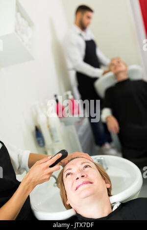 Friseur ist das Waschen der erwachsenen Frau Kopf in einem Waschbecken im barbershop Stockfoto