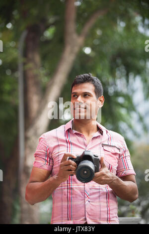 Portrait von Happy indischen Mann die Bilder mit einer Kamera in der Stadt. Asiatische Fotograf Aufnahmen im Freien mit Digitalkamera. Stockfoto