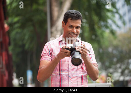 Portrait von Happy indischen Mann die Bilder mit einer Kamera in der Stadt. Asiatische Fotograf Aufnahmen im Freien mit Digitalkamera. Stockfoto